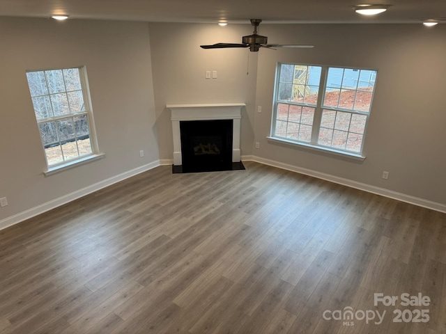 unfurnished living room featuring a fireplace with flush hearth, dark wood-style floors, baseboards, and ceiling fan