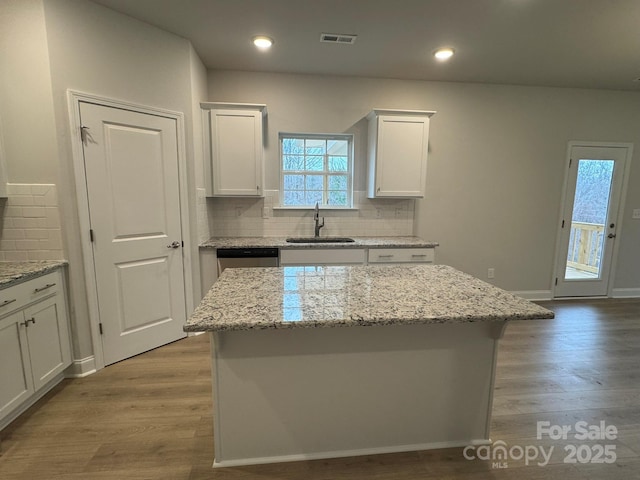 kitchen featuring light wood finished floors, white cabinets, stainless steel dishwasher, and a sink