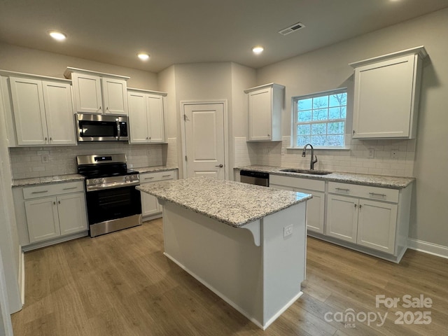 kitchen with visible vents, a center island, light wood-style flooring, stainless steel appliances, and a sink