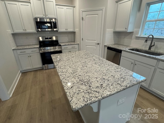 kitchen with light stone counters, wood finished floors, a sink, appliances with stainless steel finishes, and a center island