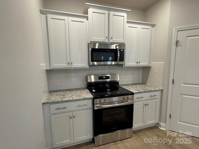 kitchen with light wood-type flooring, tasteful backsplash, white cabinetry, stainless steel appliances, and light stone countertops