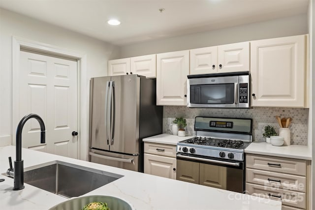 kitchen featuring light stone counters, a sink, white cabinets, appliances with stainless steel finishes, and backsplash