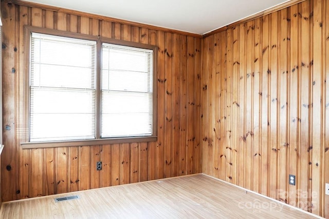 spare room featuring a wealth of natural light, visible vents, wood finished floors, and wooden walls