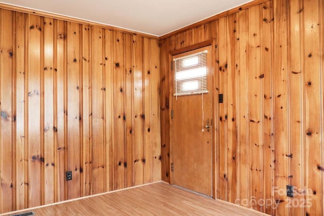 unfurnished room with light wood-style floors and wooden walls