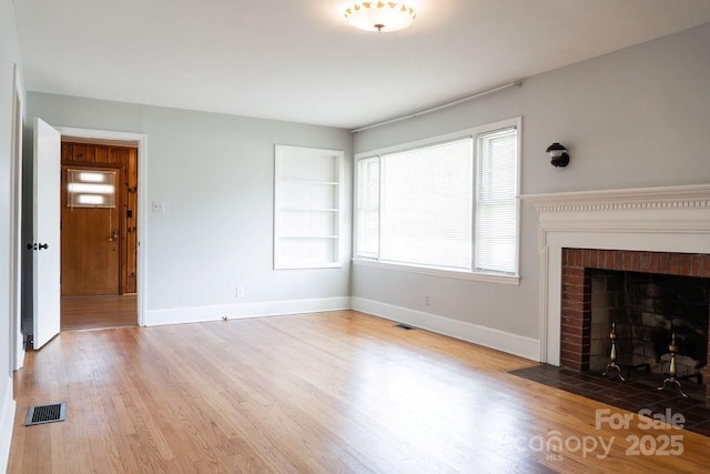 unfurnished living room featuring a brick fireplace, baseboards, visible vents, and wood finished floors