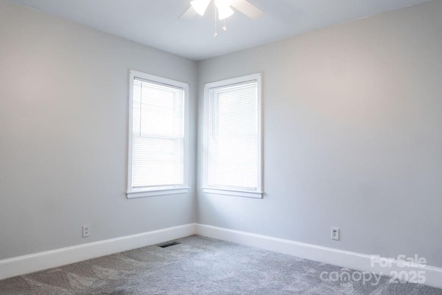 carpeted spare room featuring plenty of natural light, visible vents, baseboards, and a ceiling fan