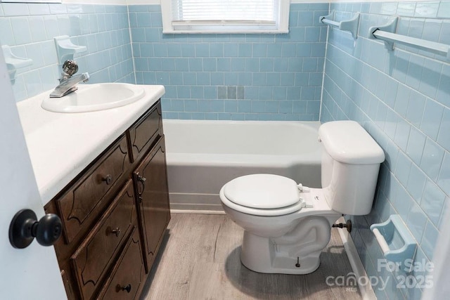 full bath featuring tile walls, toilet, wood finished floors, vanity, and a washtub