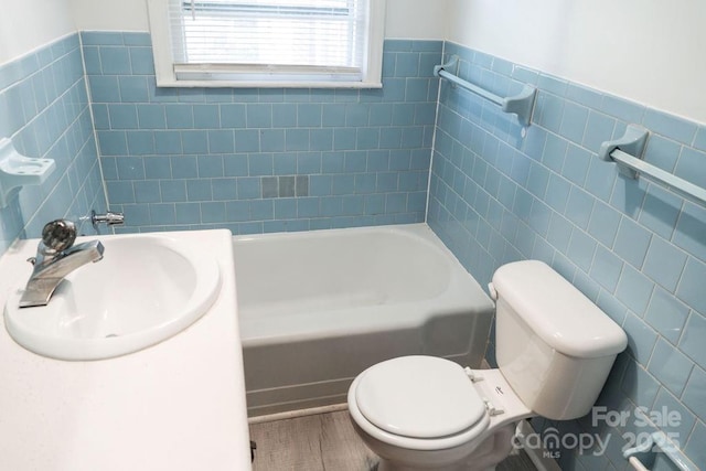 bathroom with tile walls, toilet, wainscoting, a sink, and a bathing tub