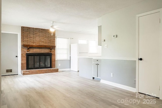 unfurnished living room featuring a textured ceiling, visible vents, light wood-style flooring, and a ceiling fan