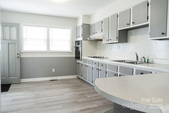 kitchen featuring a sink, stainless steel oven, light wood-type flooring, under cabinet range hood, and gray cabinetry