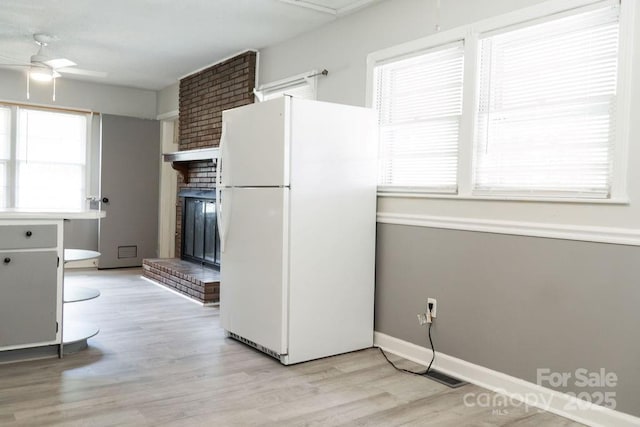 kitchen with freestanding refrigerator, a fireplace, baseboards, ceiling fan, and light wood-style floors