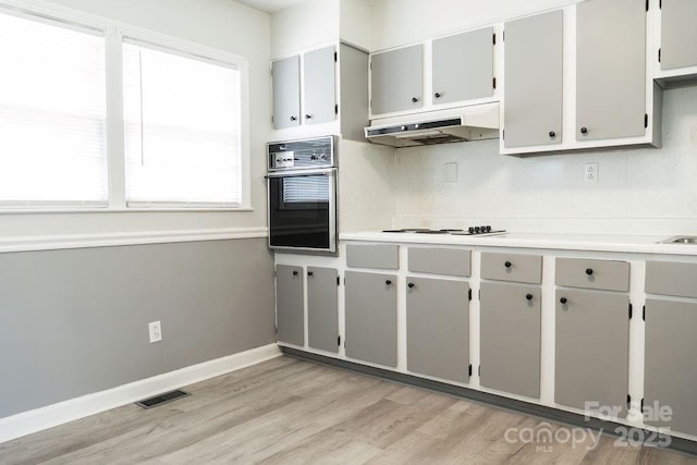 kitchen with oven, visible vents, under cabinet range hood, light countertops, and light wood-style floors