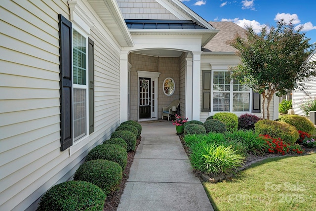 doorway to property with covered porch and a shingled roof