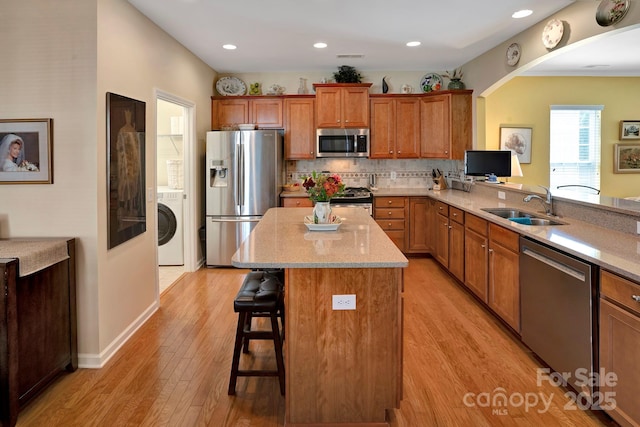 kitchen featuring brown cabinetry, a breakfast bar, washer / dryer, a sink, and appliances with stainless steel finishes