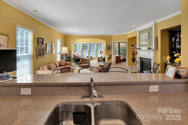 kitchen with a glass covered fireplace, crown molding, visible vents, and a sink