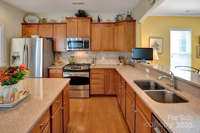 kitchen featuring brown cabinets, a sink, backsplash, appliances with stainless steel finishes, and light wood finished floors