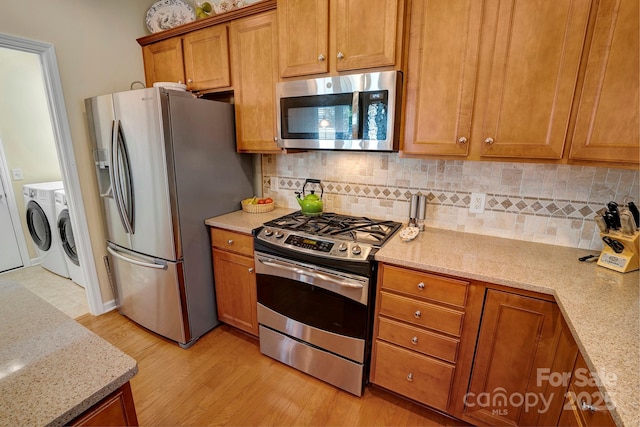 kitchen with washer and dryer, backsplash, stainless steel appliances, brown cabinetry, and light wood finished floors