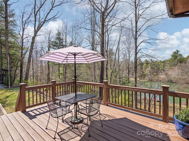 wooden deck with a view of trees and outdoor dining space