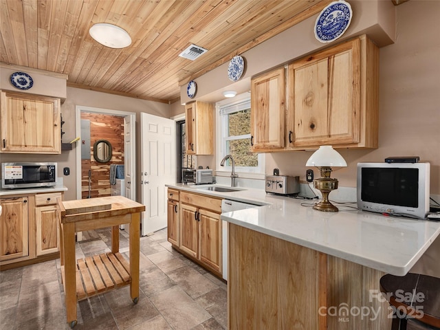 kitchen featuring light brown cabinets, a sink, stainless steel microwave, light countertops, and wood ceiling