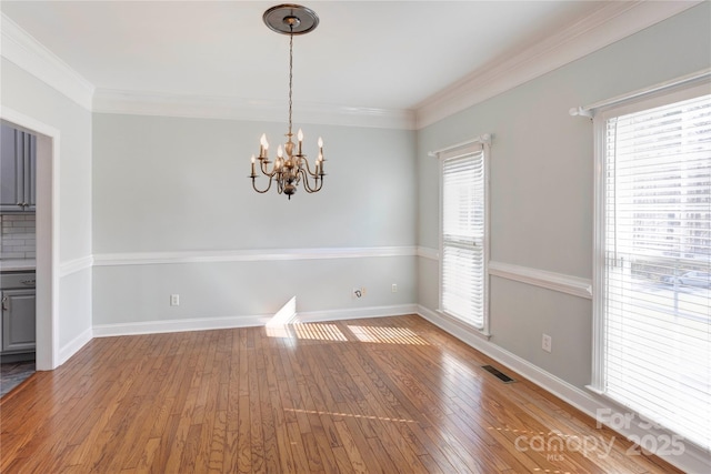 unfurnished dining area featuring visible vents, a notable chandelier, light wood-style flooring, and crown molding