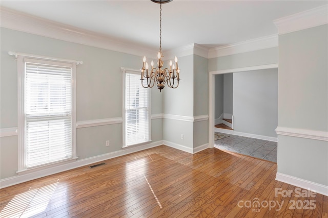 empty room with light wood finished floors, visible vents, crown molding, baseboards, and a notable chandelier