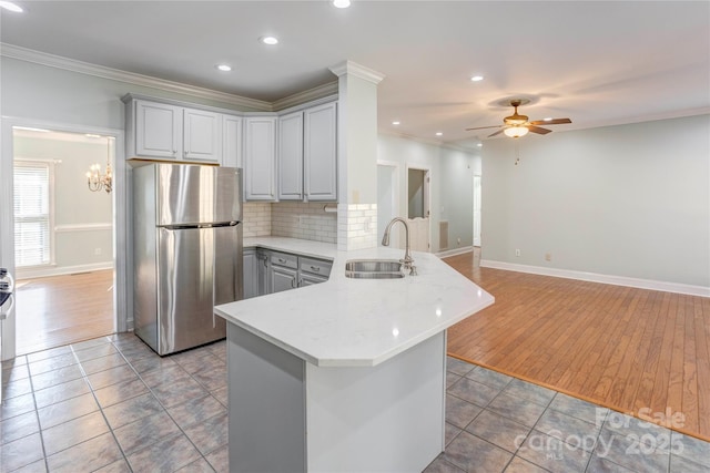 kitchen featuring a peninsula, freestanding refrigerator, ornamental molding, gray cabinetry, and a sink