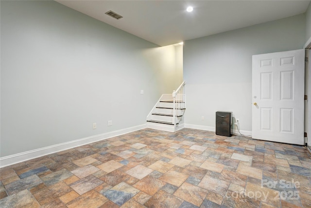 below grade area with stone finish floor, stairway, visible vents, and baseboards