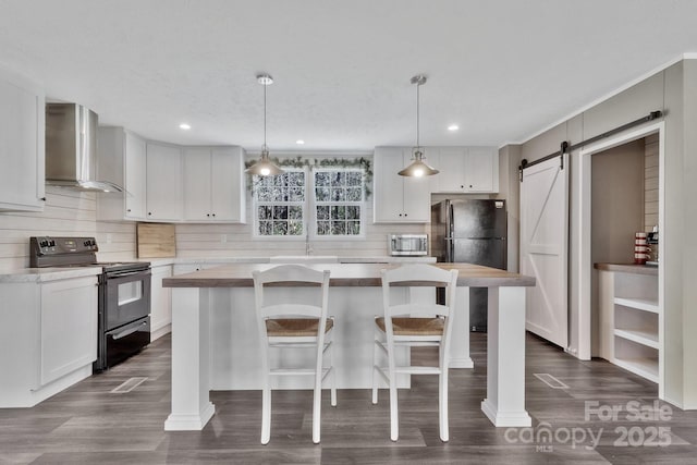 kitchen featuring black appliances, backsplash, a center island, a barn door, and wall chimney exhaust hood