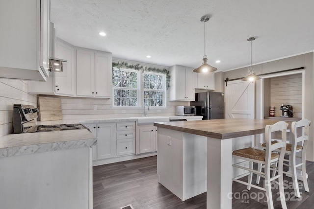 kitchen featuring electric range, a breakfast bar, freestanding refrigerator, a barn door, and butcher block counters
