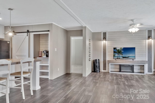 living area with a ceiling fan, a barn door, wood finished floors, and a textured ceiling