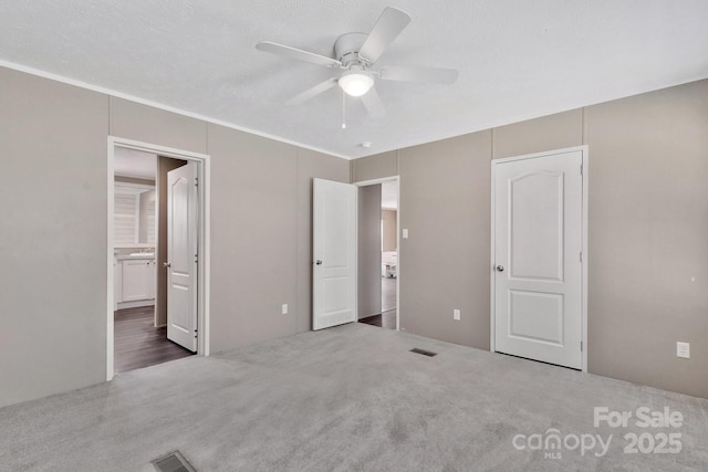 unfurnished bedroom with visible vents, a ceiling fan, ensuite bath, and carpet flooring