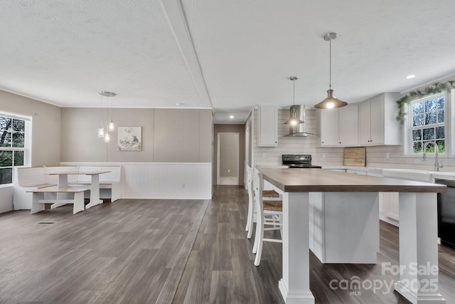 kitchen with a wealth of natural light, black / electric stove, wall chimney exhaust hood, and dark wood-type flooring