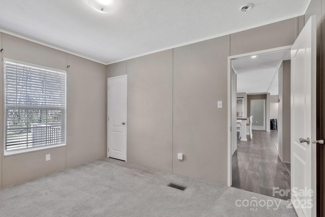 unfurnished bedroom with carpet, visible vents, and a textured ceiling