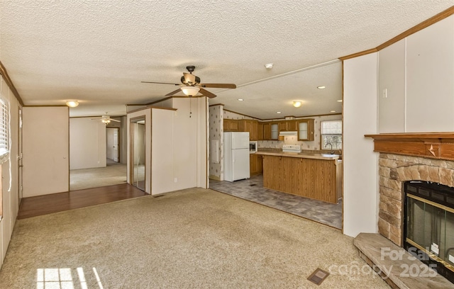 unfurnished living room featuring a ceiling fan, a stone fireplace, carpet, and a textured ceiling