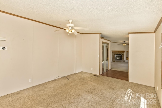 unfurnished room with a textured ceiling, visible vents, carpet, a ceiling fan, and a glass covered fireplace