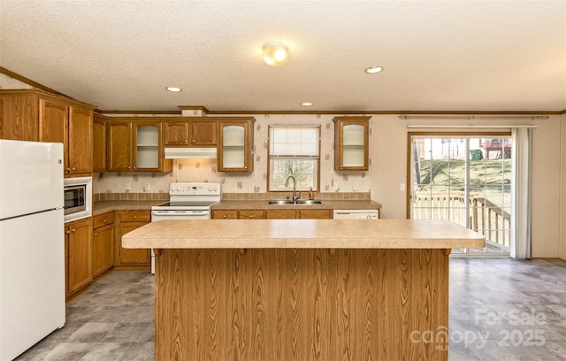 kitchen featuring a sink, a center island, under cabinet range hood, white appliances, and a healthy amount of sunlight