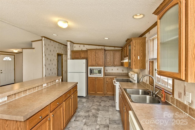 kitchen with under cabinet range hood, a sink, brown cabinets, and white appliances