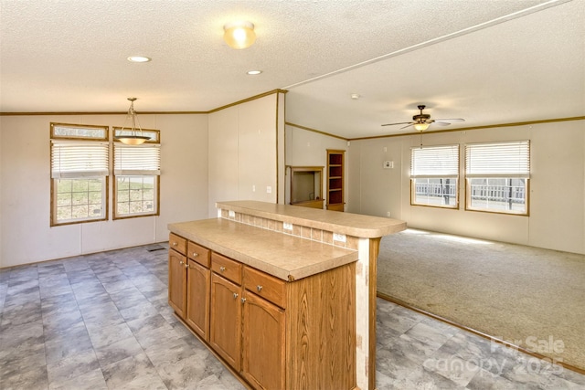 kitchen with crown molding, a textured ceiling, a center island, brown cabinetry, and ceiling fan