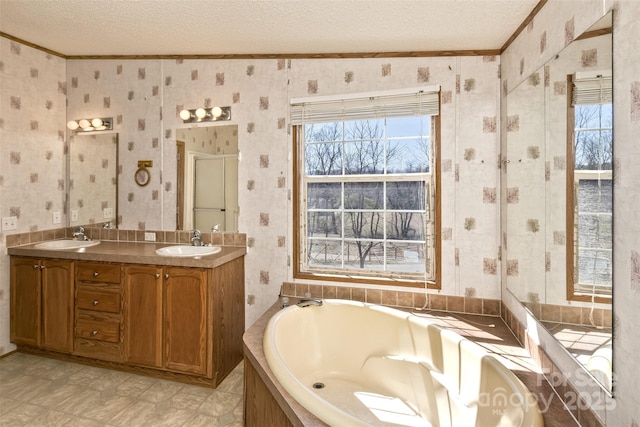 bathroom featuring a sink, a textured ceiling, wallpapered walls, and a garden tub