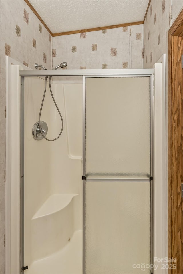 full bathroom featuring wallpapered walls, a textured ceiling, and a shower stall