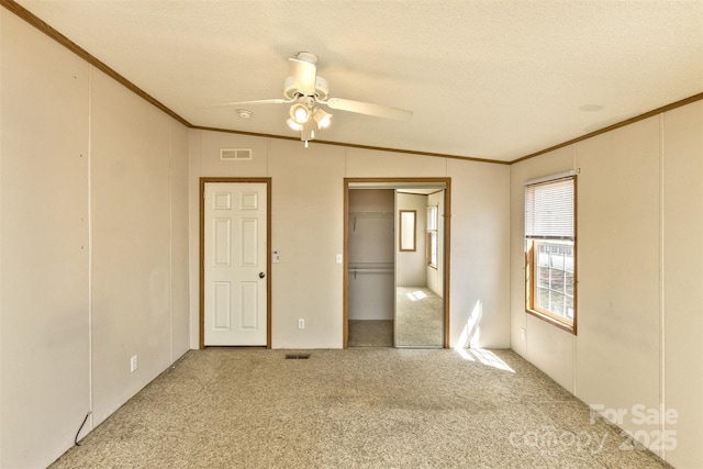 unfurnished bedroom with ornamental molding, carpet, ceiling fan, and visible vents