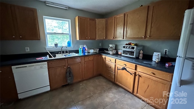 kitchen featuring dark countertops, white appliances, light tile patterned flooring, and a sink