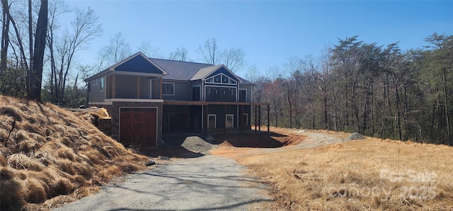 rustic home featuring stone siding, a wooded view, and driveway