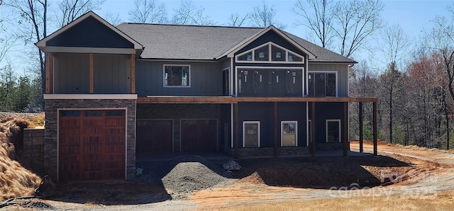 view of front of house with stone siding, an attached garage, a shingled roof, and board and batten siding