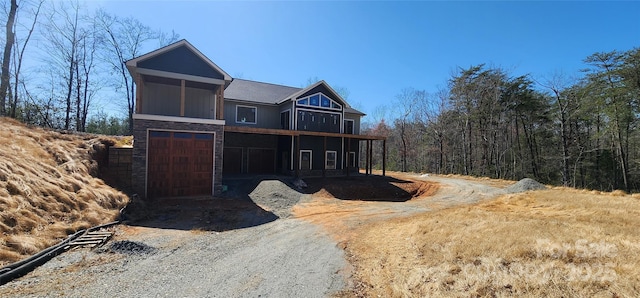 view of front of home featuring a garage, stone siding, a balcony, and driveway