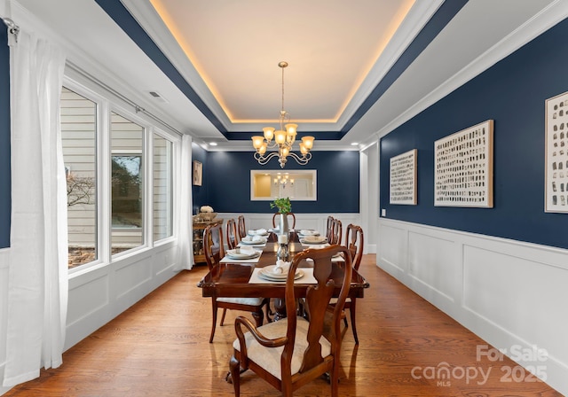 dining space with visible vents, a decorative wall, wood finished floors, a notable chandelier, and a raised ceiling