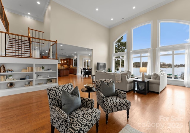 living area with stairway, wood finished floors, a towering ceiling, and ornamental molding