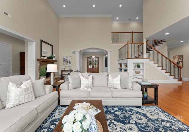 living room featuring stairs, ornamental molding, wood finished floors, arched walkways, and ornate columns