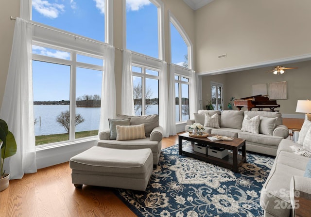 living area with ceiling fan, a wealth of natural light, wood finished floors, and a water view