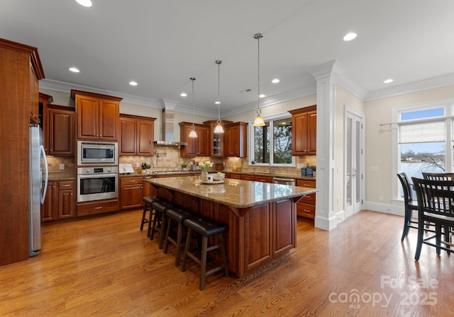 kitchen featuring light wood finished floors, stainless steel appliances, a kitchen bar, wall chimney range hood, and a center island